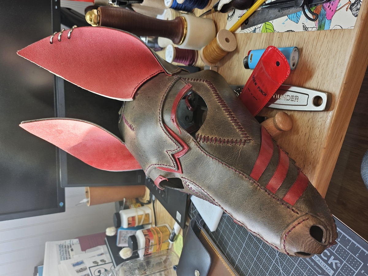 A brown/grey leather mask of a long snouted dog with visible teeth and red detailing.