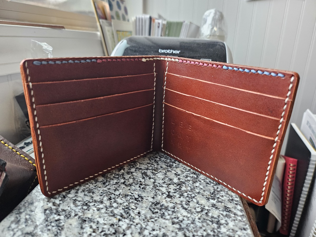 A brown leather wallet with a subtle trans flag stitching across the top.