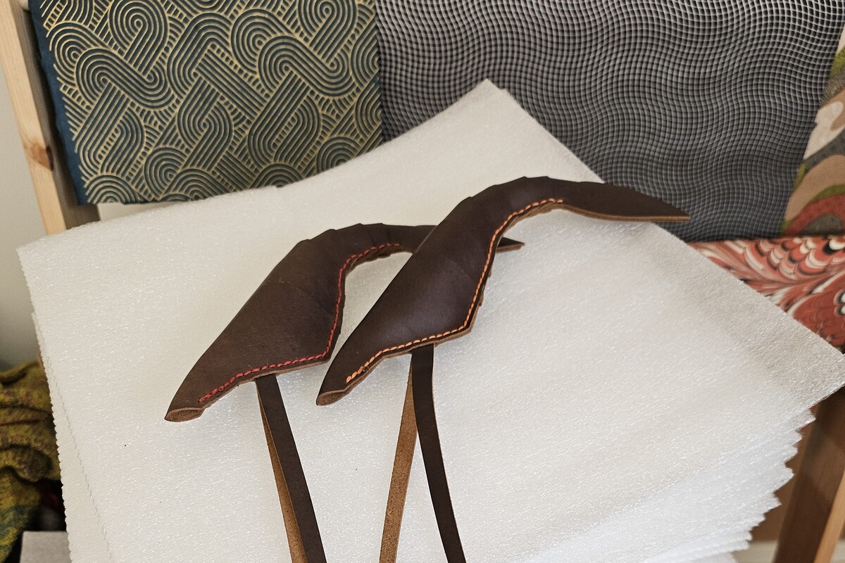 Two leather shrimp-shaped cat toys. They have long dangly antennae and are stitched in red and orange.