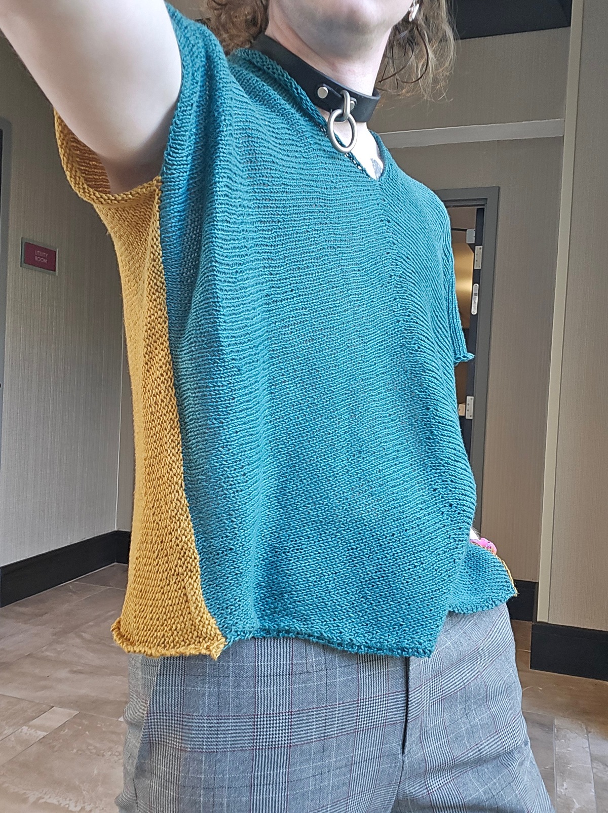 someone's torso in a knitted short sleeve shirt. the front is teal, and the bit of back we can see is mustard yellow. looking closely, it's notable that the stitches are turned 90 degrees from a standard knit garment.