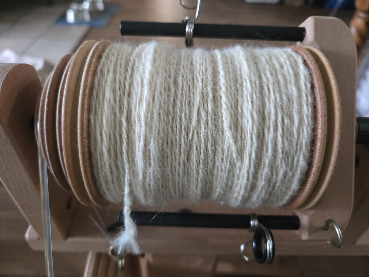 a spinning wheel bobbin full of undyed white handspun yarn in about a sport or DK weight.