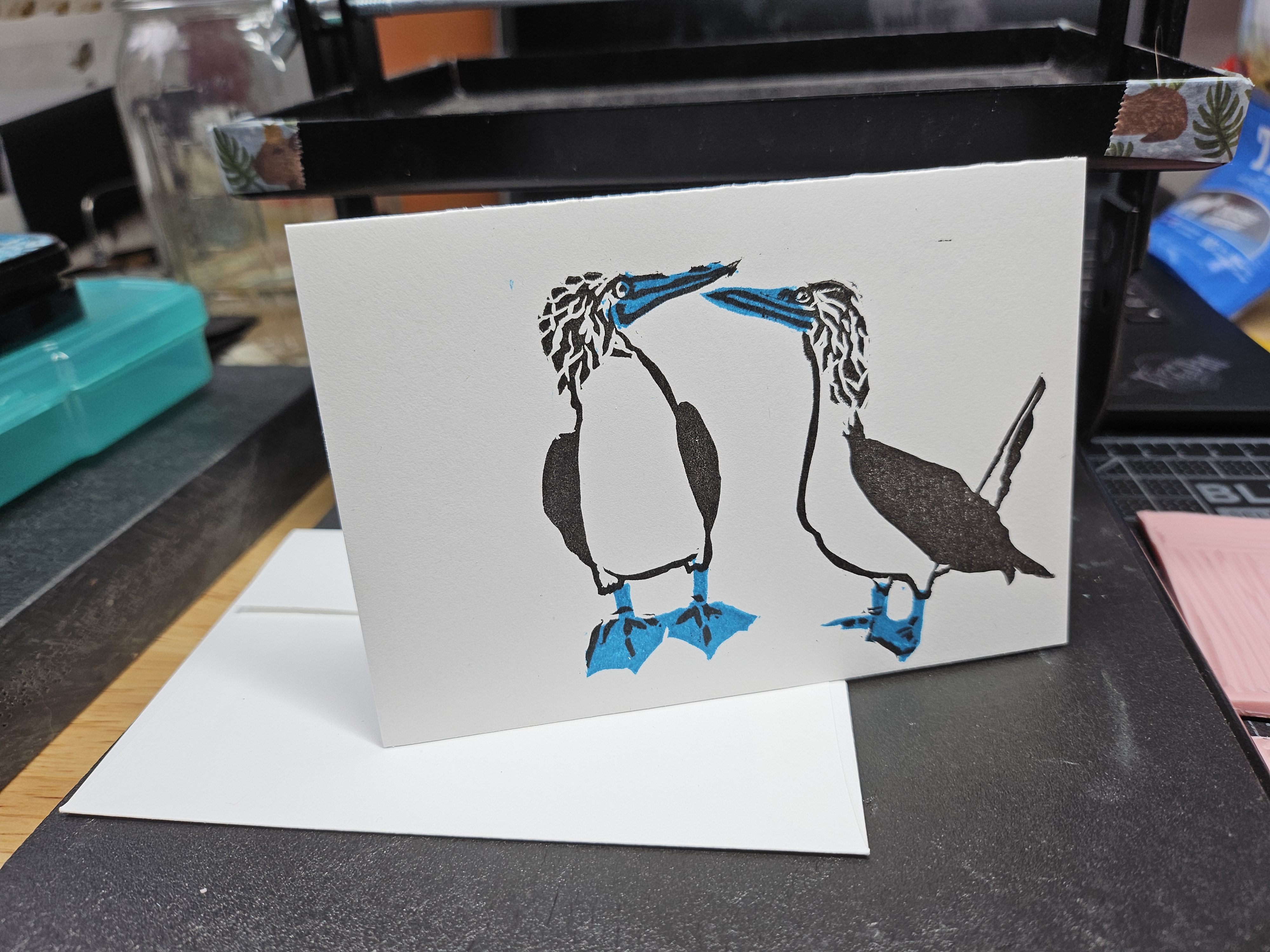 A landscape-oriented white card with a two-color print of a blue-footed booby.