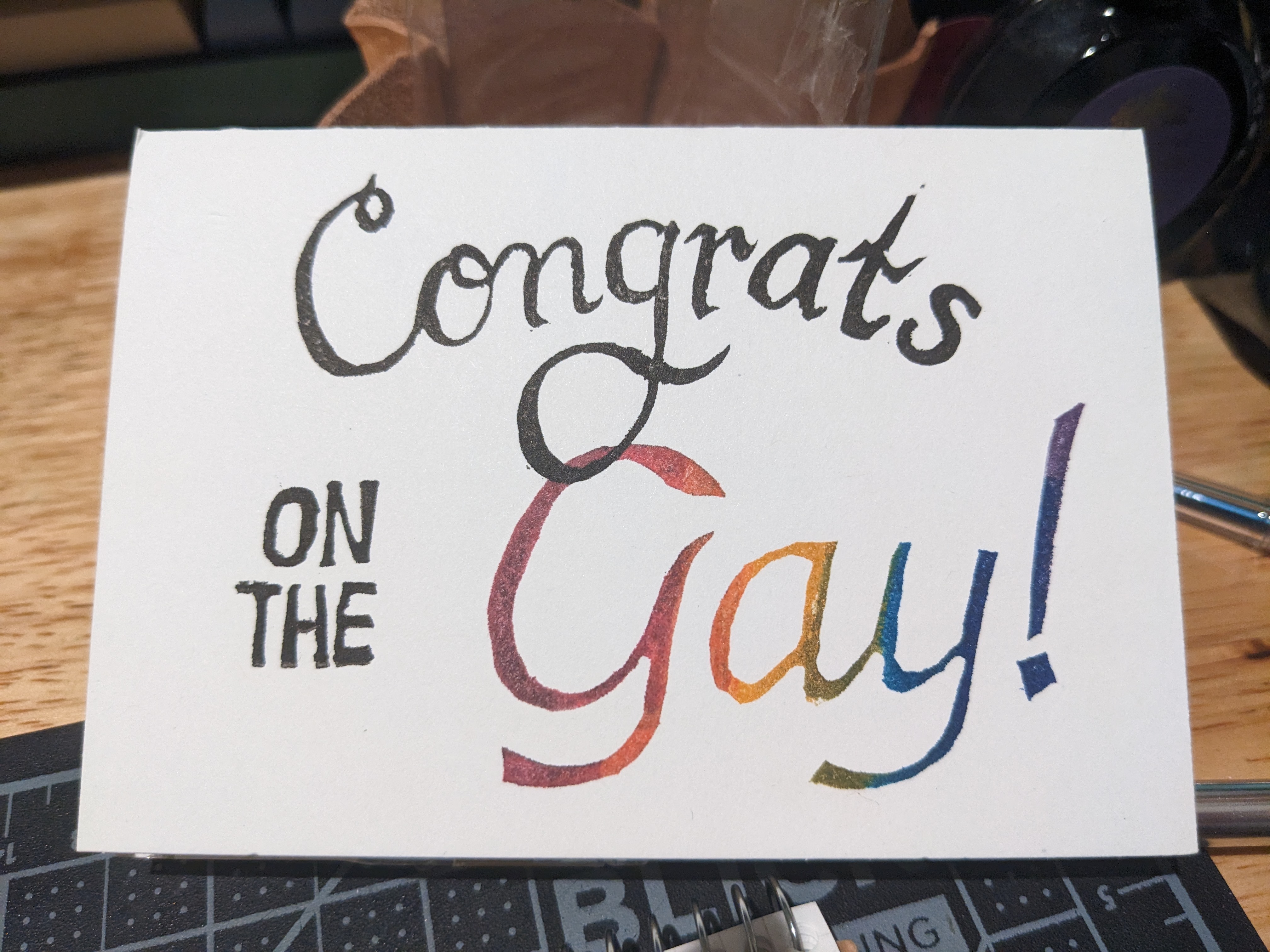 A greeting card reading, in black. 'Congrats on the,' and then, in rainbow, 'Gay!'