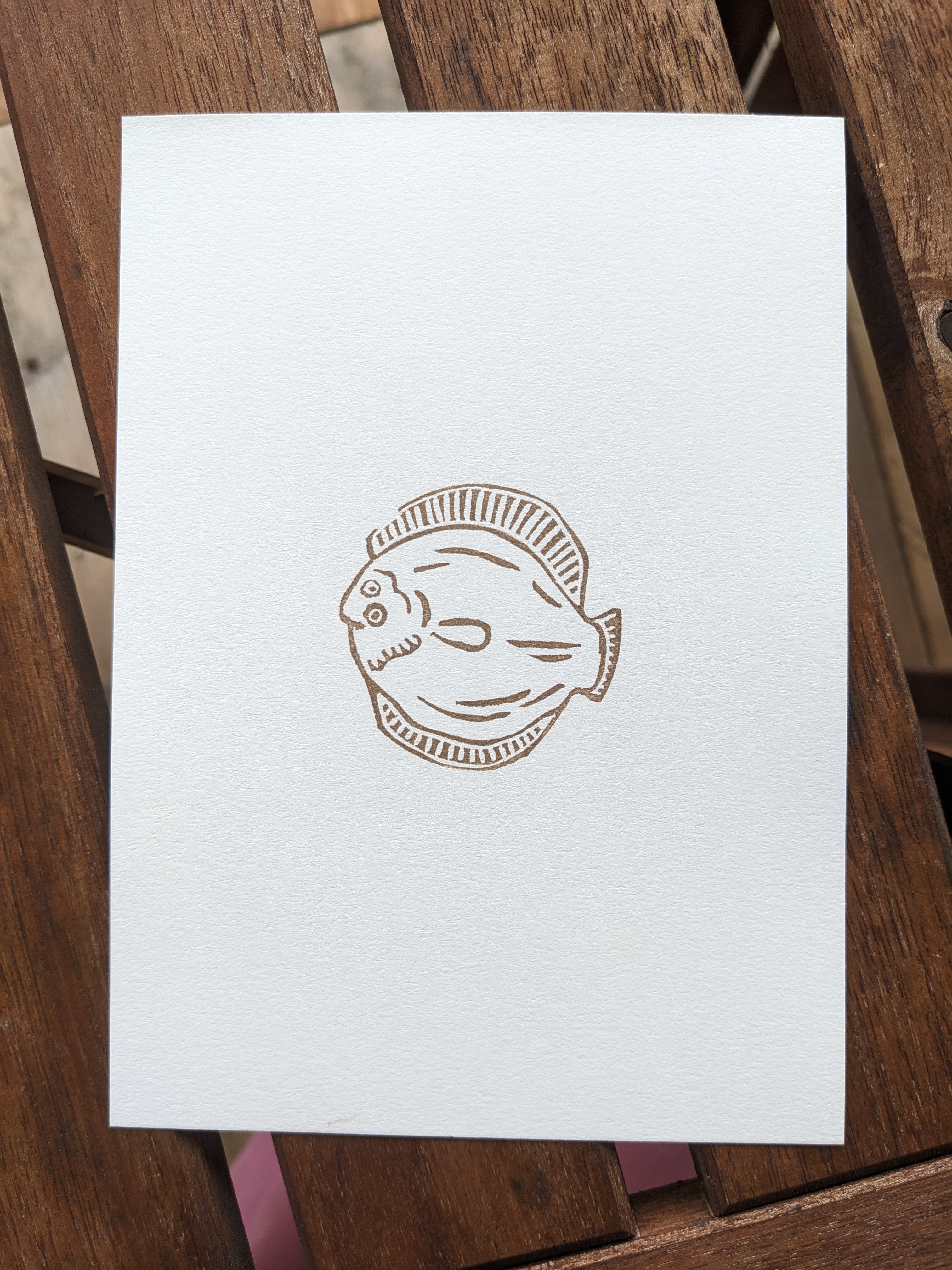 A print of a simple flatfish design inked in sepia.