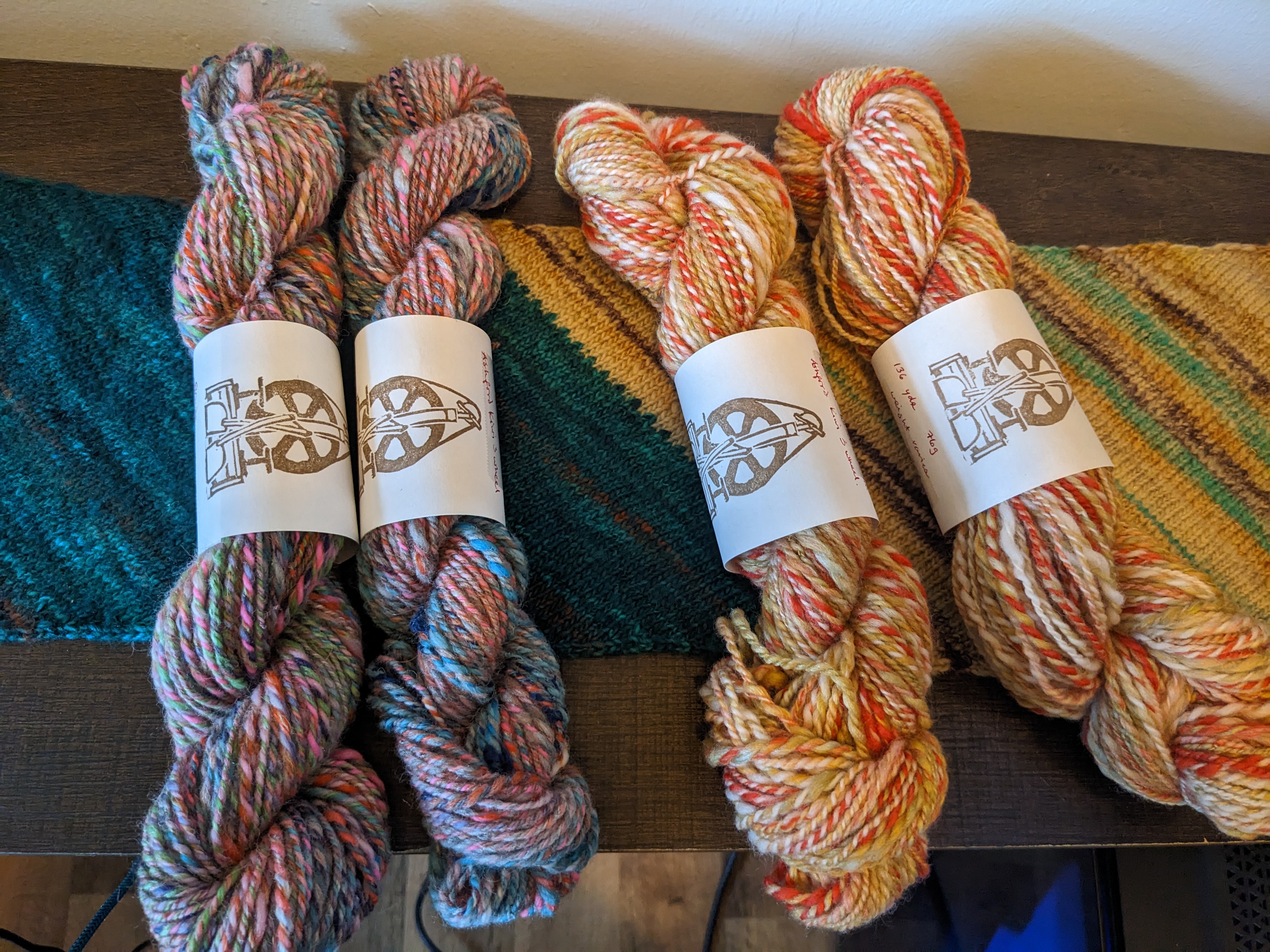 4 skeins of handspun yarn, two in a somewhat pastel multicolor and two in a blend of orange, gold, and white.
