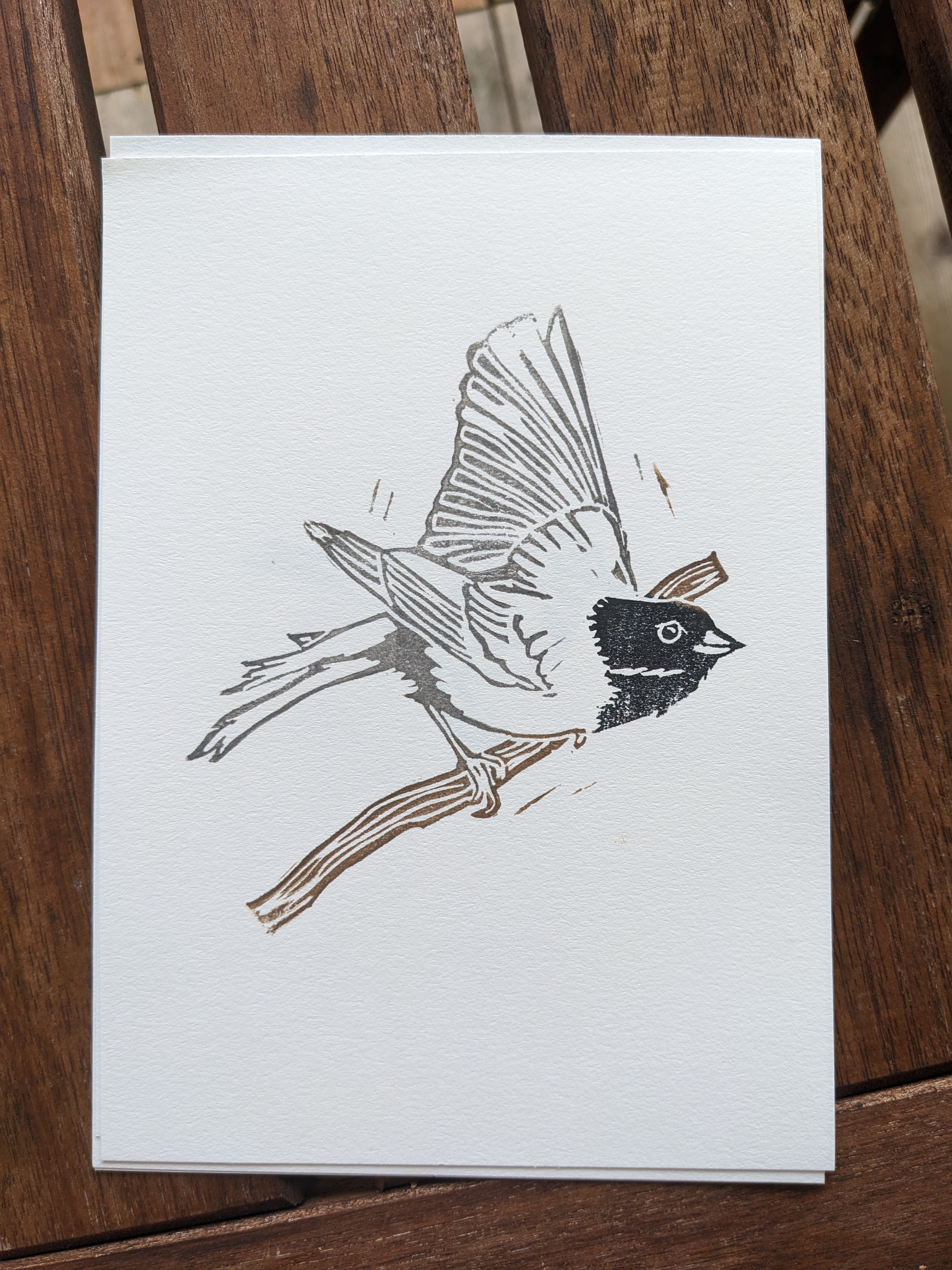 A print of a junco mid-takeoff from a branch. Eir head is inked in black, body in gray, and the branch in sepia.