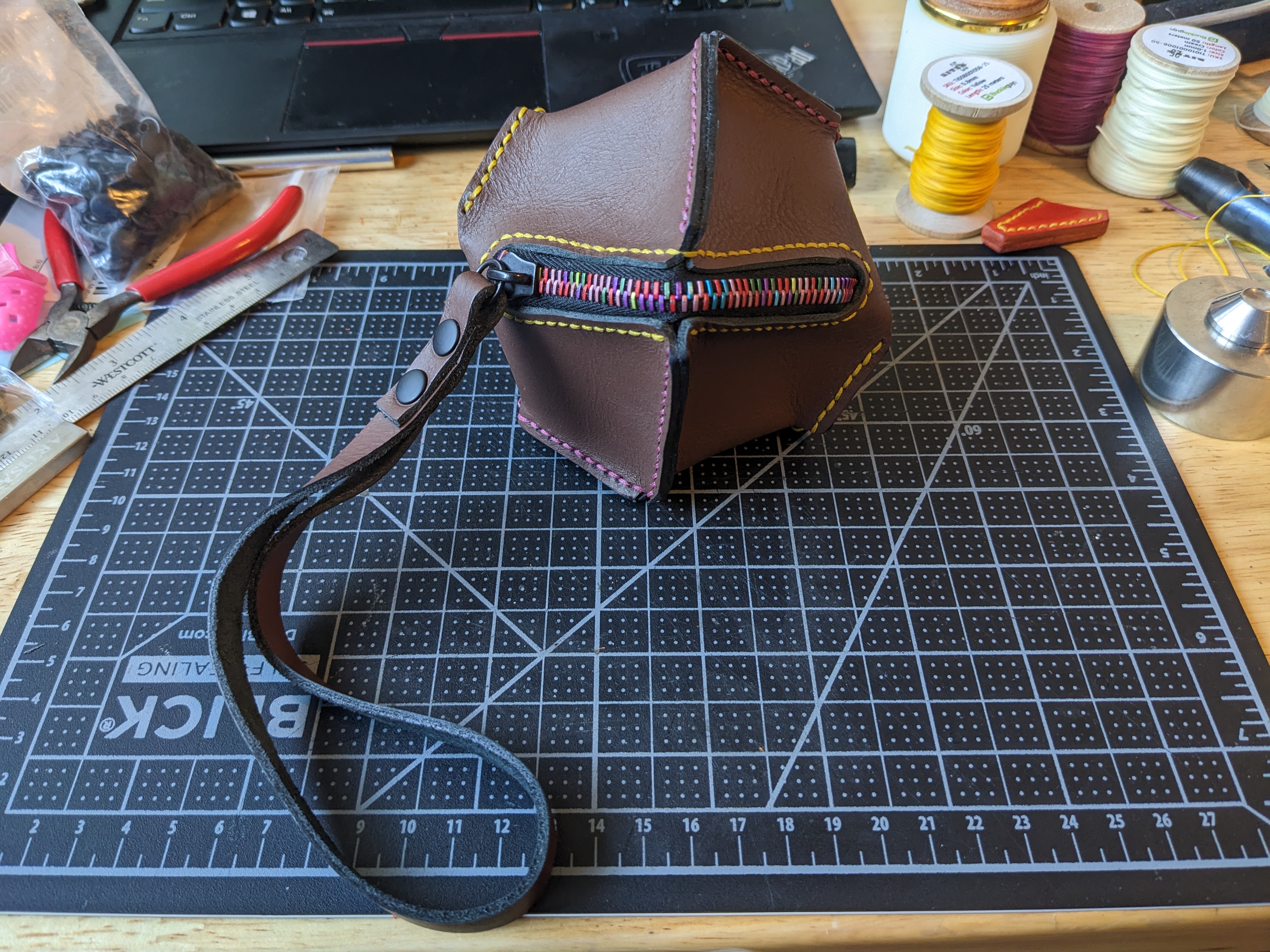A leather pouch shaped a bit like a d10 but with eight sides. It has a rainbow zippered opening and a wristlet strap.