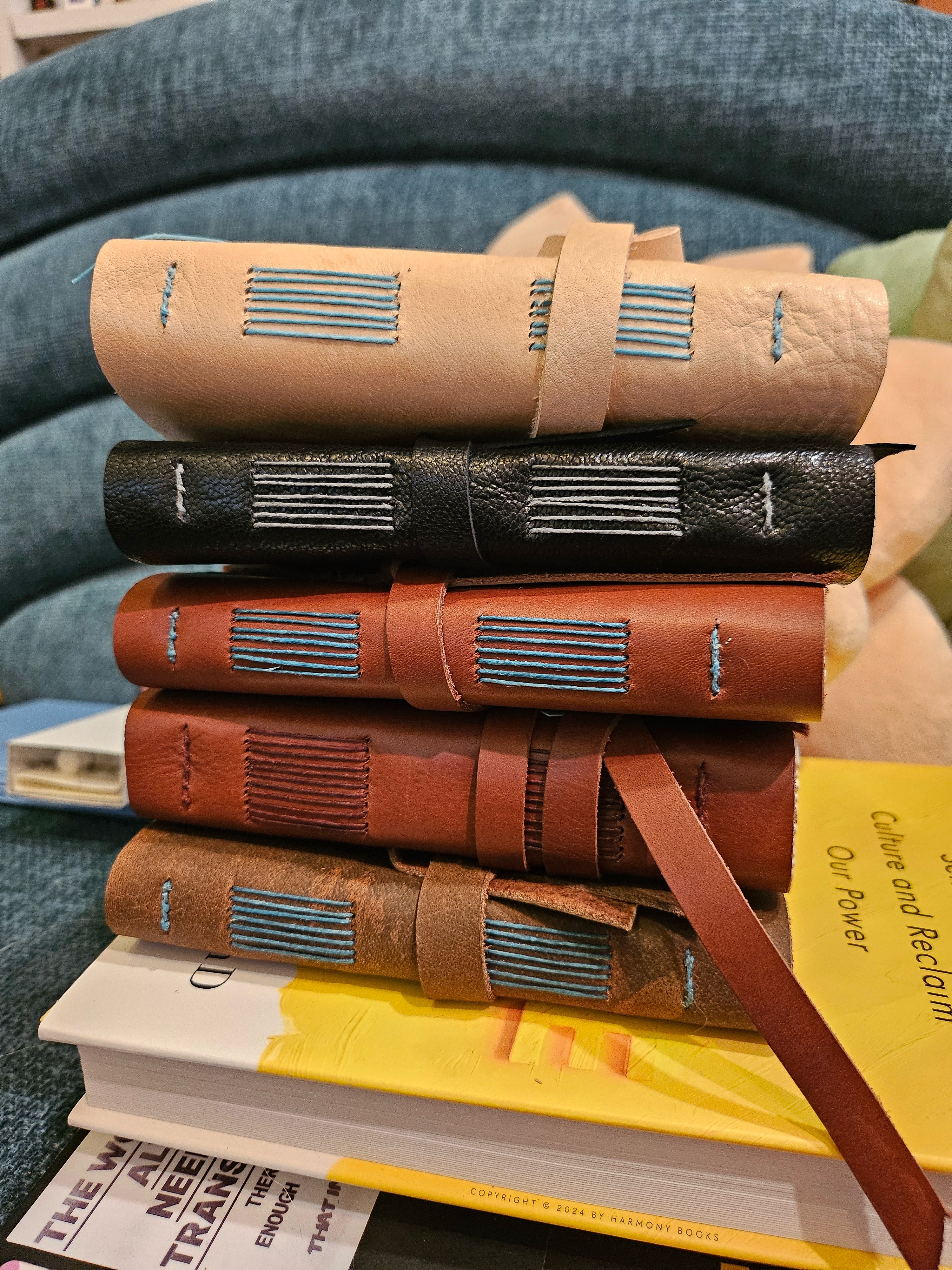 A stack of hand-bound journals showing long stitches aligned with the spines. They are leather bound and have tie closures.