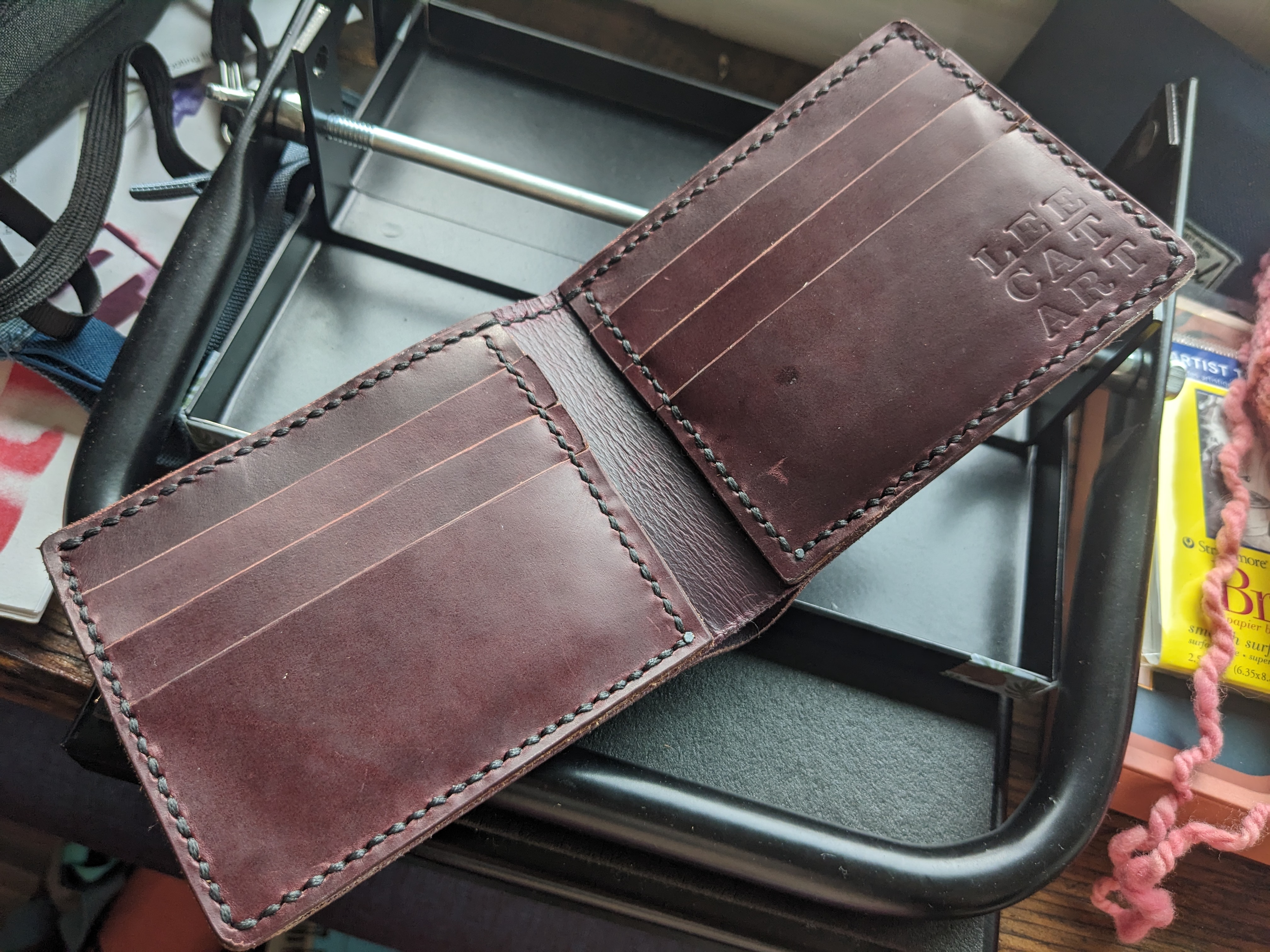 A hand stitched full grain leather bifold wallet in dark plum leather. It has a main bill pocket and a symmetrical interior with a hidden pocket and 3 card pockets on each side.