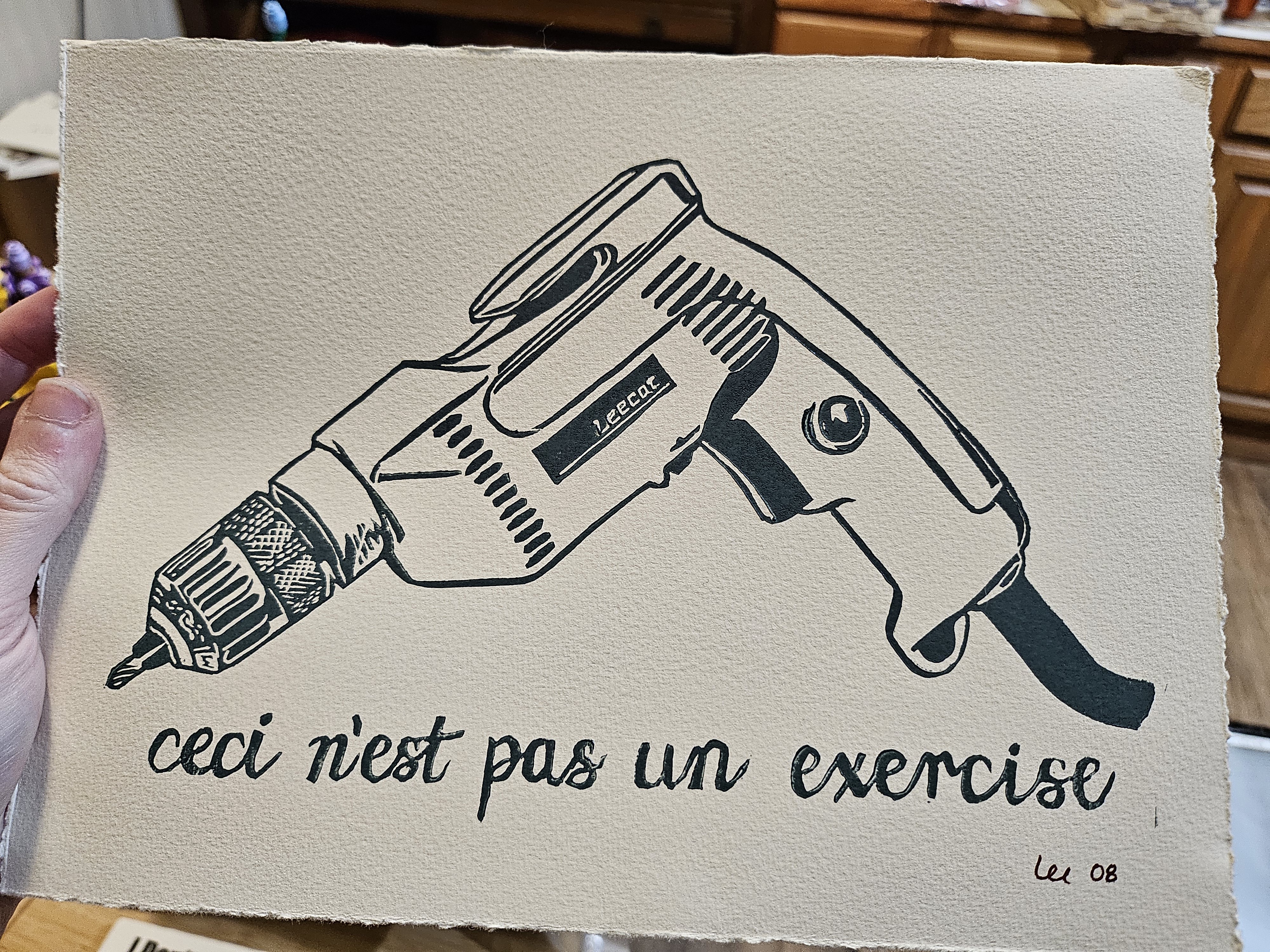 A print in dark teal ink depicting a power drill with text in cursive below that reads 'ceci n'est pas un exercice' or 'this is not a drill'