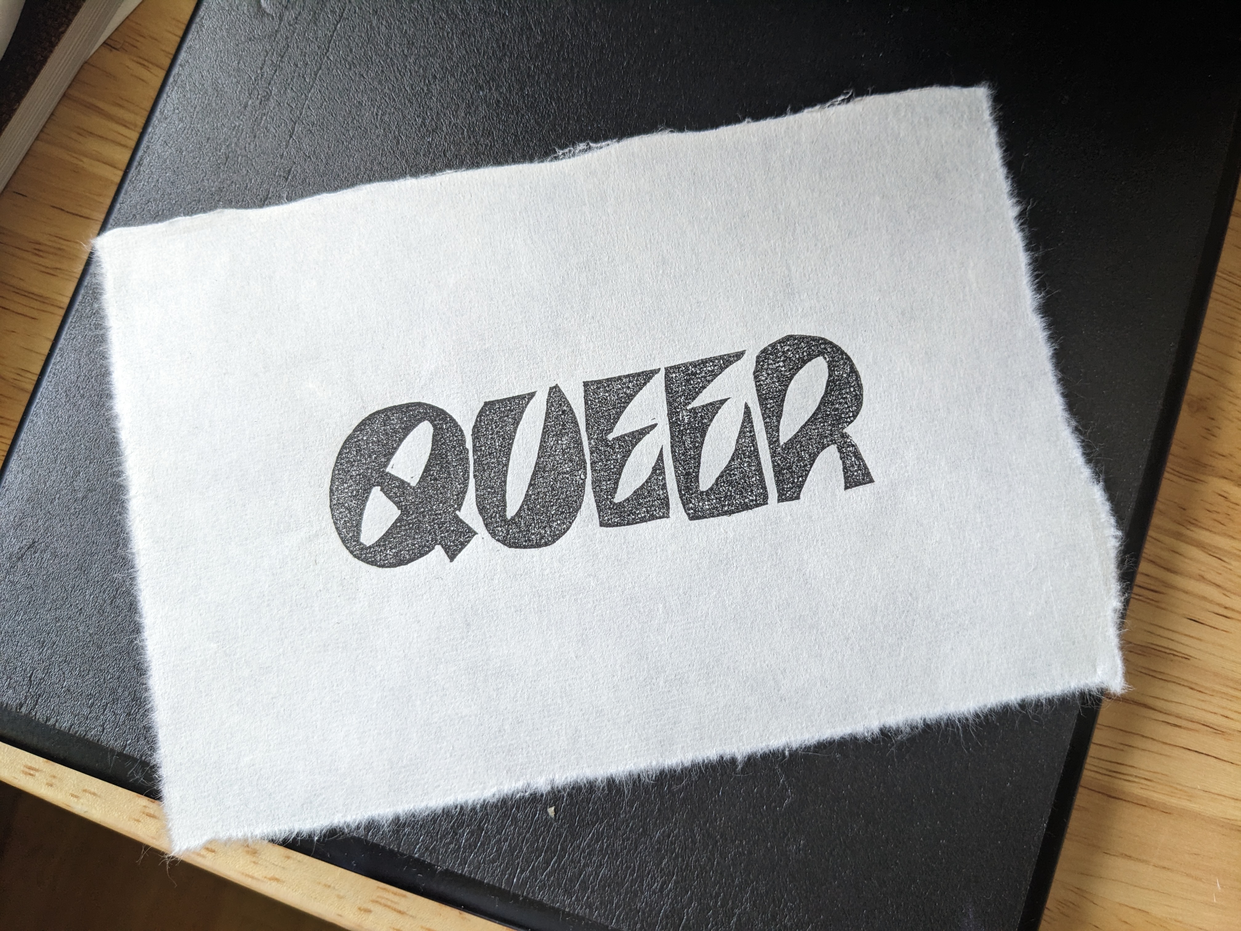 A print of the word queer in black ink. The letters are rounded with elongated oval negative space.