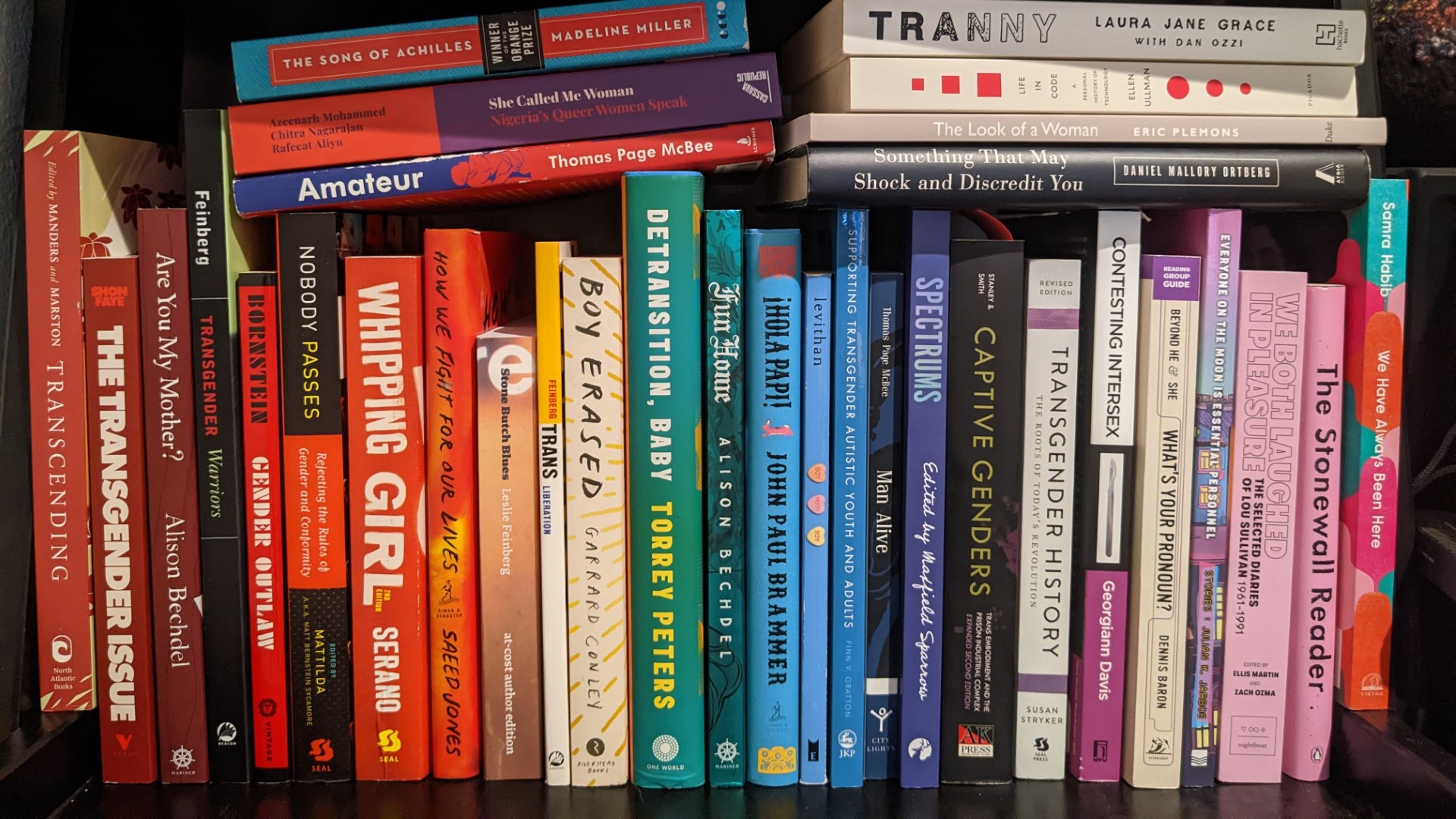A bookshelf with a variety of books on LGBTQ+ themes, arranged roughly in rainbow order