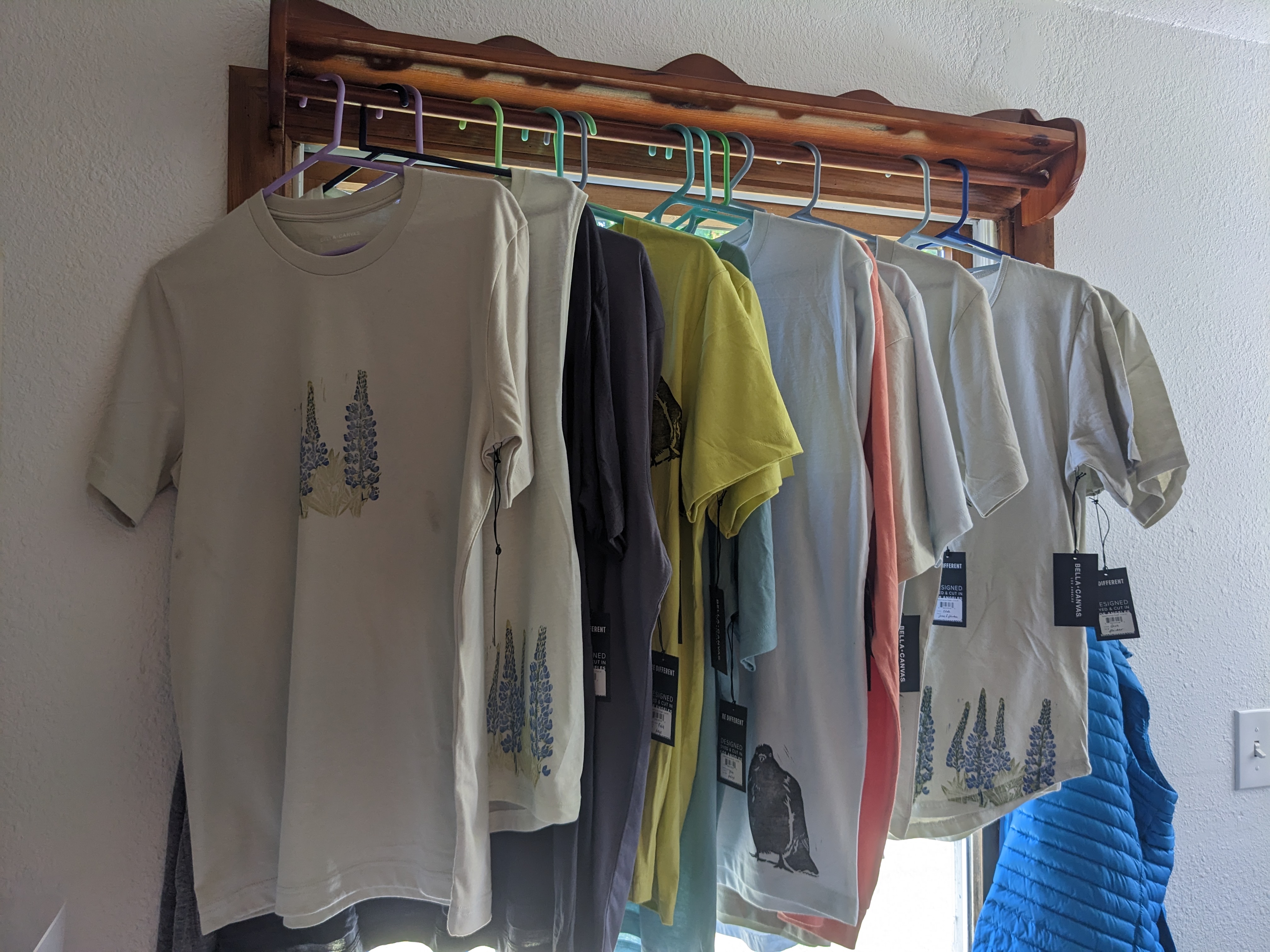 A row of shirts hanging in front of a window, with a variety of hand-printed designs.