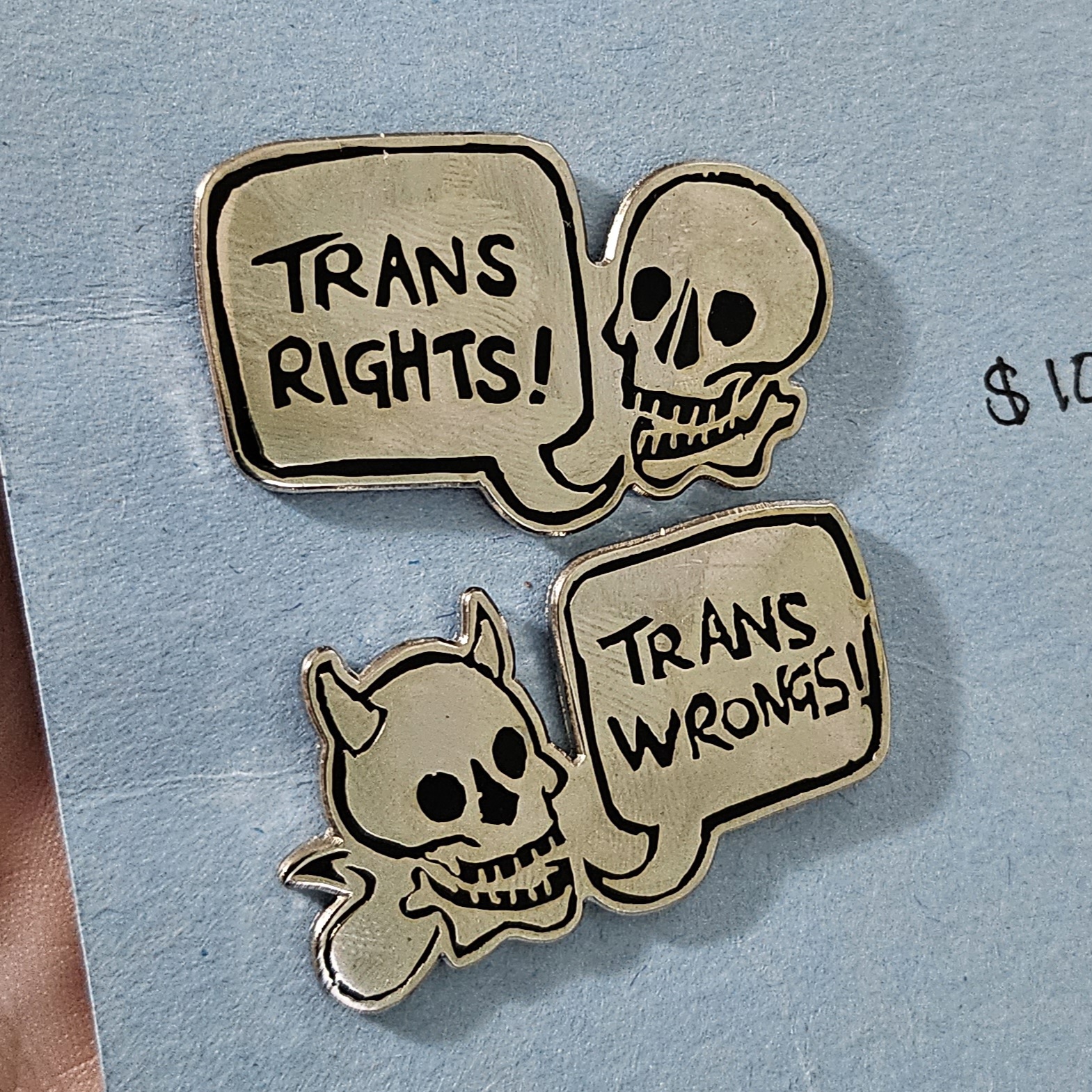 Two hard enamel pins in my trans rights and trans wrongs skulls designs.