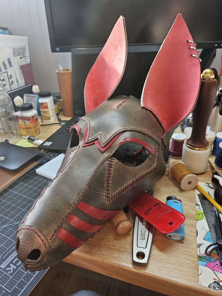 A brown/grey leather mask of a long snouted dog with visible teeth and red detailing.