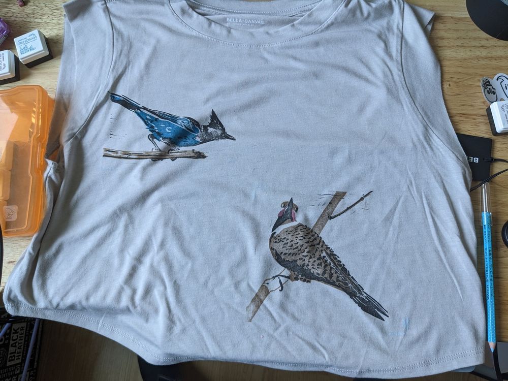 A shirt laid out on my desk after being printed with my jay and flicker prints. There are ink pads and other tools scattered around.